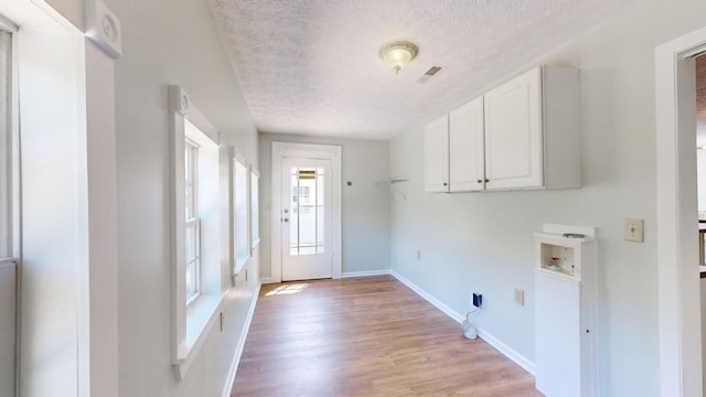 washroom featuring hookup for a washing machine, cabinets, a textured ceiling, and light hardwood / wood-style floors