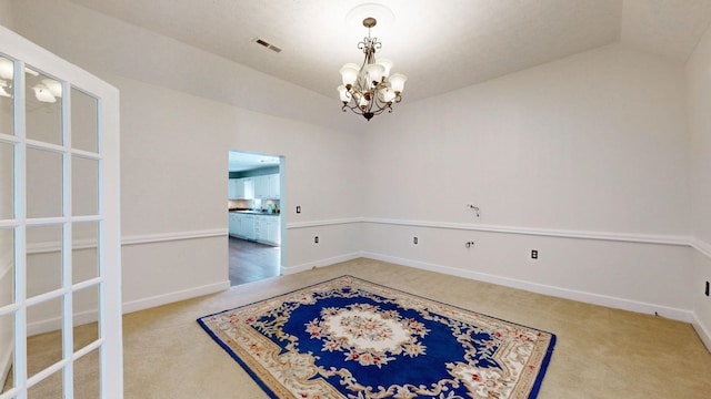 carpeted spare room featuring lofted ceiling and an inviting chandelier