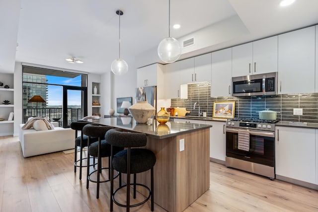 kitchen featuring pendant lighting, backsplash, sink, white cabinetry, and stainless steel appliances