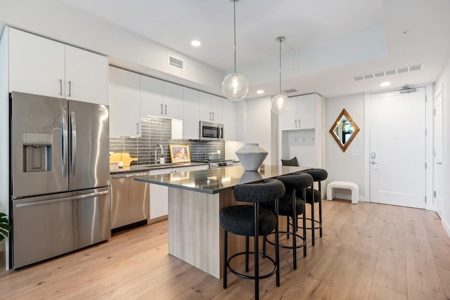 kitchen featuring white cabinetry, a center island, light hardwood / wood-style flooring, pendant lighting, and appliances with stainless steel finishes