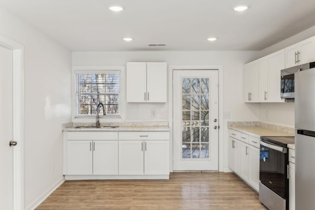 kitchen with white cabinets, appliances with stainless steel finishes, light hardwood / wood-style floors, and sink