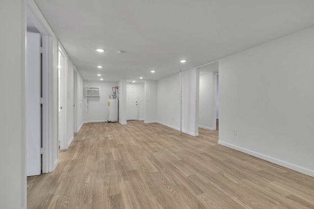 basement with a wall mounted air conditioner, light hardwood / wood-style floors, and water heater