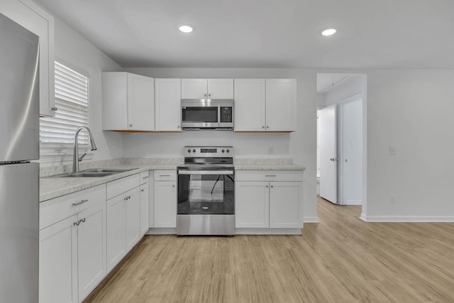 kitchen featuring light stone countertops, sink, appliances with stainless steel finishes, white cabinets, and light wood-type flooring