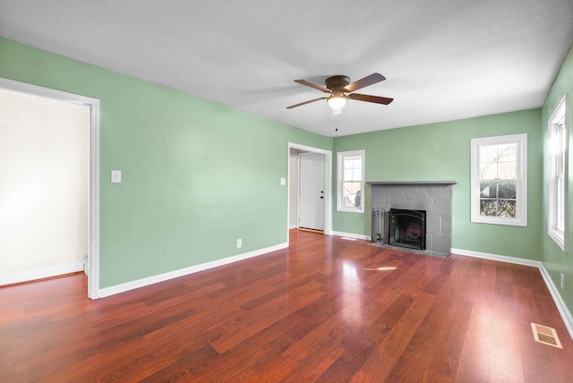 unfurnished living room with ceiling fan, a fireplace, a wealth of natural light, and hardwood / wood-style floors