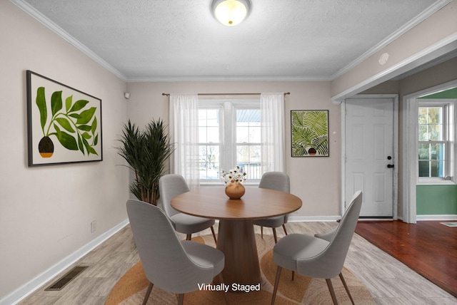 dining room with a textured ceiling, ornamental molding, and light hardwood / wood-style flooring