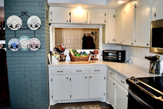 kitchen featuring white cabinetry, brick wall, black range with electric stovetop, and decorative backsplash