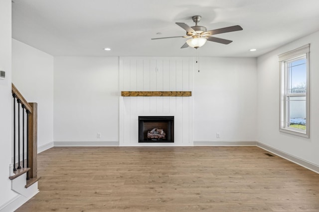 unfurnished living room featuring ceiling fan, a large fireplace, and light hardwood / wood-style flooring