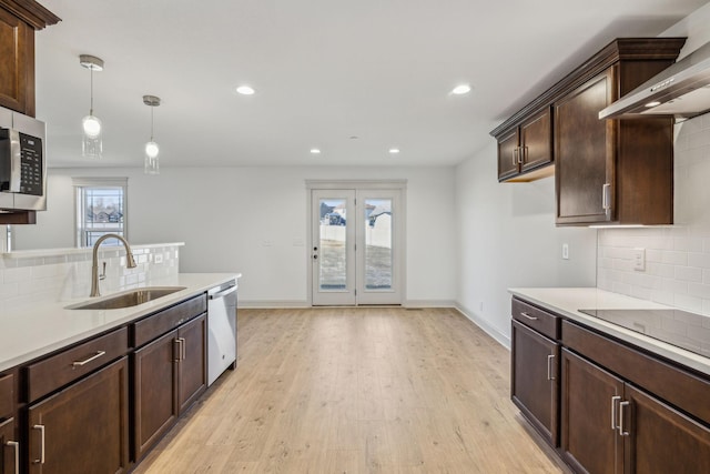 kitchen with sink, wall chimney range hood, light hardwood / wood-style floors, pendant lighting, and appliances with stainless steel finishes