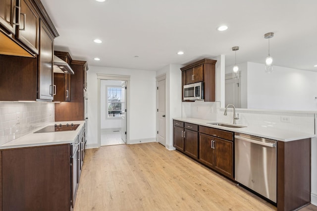 kitchen featuring light wood-type flooring, dark brown cabinets, stainless steel appliances, sink, and decorative light fixtures