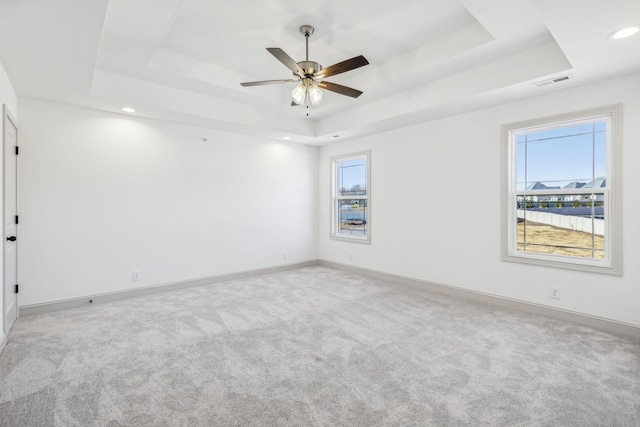 spare room featuring a tray ceiling, ceiling fan, and light colored carpet