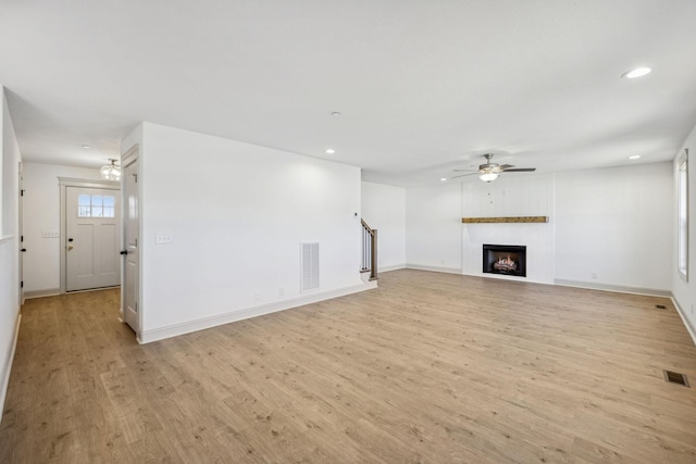 unfurnished living room with ceiling fan, a large fireplace, and light hardwood / wood-style floors