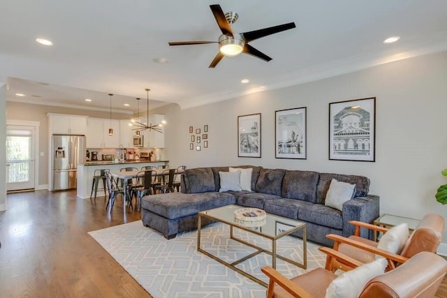 living room featuring ornamental molding, ceiling fan with notable chandelier, dark wood-type flooring, and sink