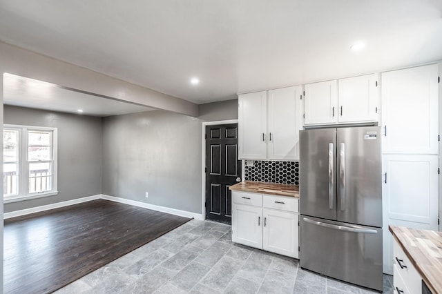 kitchen featuring white cabinetry, wooden counters, stainless steel refrigerator, and decorative backsplash