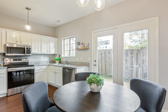 kitchen with hanging light fixtures, white cabinetry, appliances with stainless steel finishes, and light stone counters