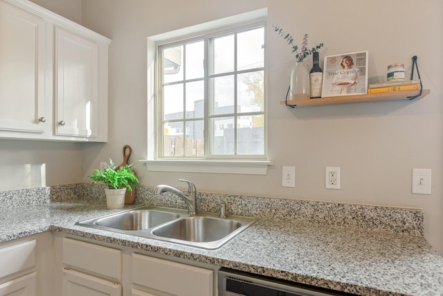 kitchen with light stone counters, plenty of natural light, sink, and white cabinets