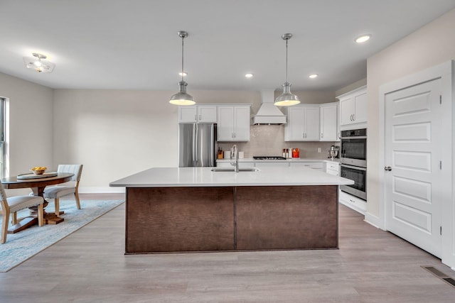 kitchen with premium range hood, white cabinets, sink, light wood-type flooring, and appliances with stainless steel finishes