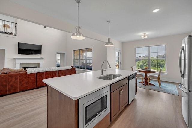 kitchen with appliances with stainless steel finishes, sink, pendant lighting, a center island with sink, and light hardwood / wood-style floors