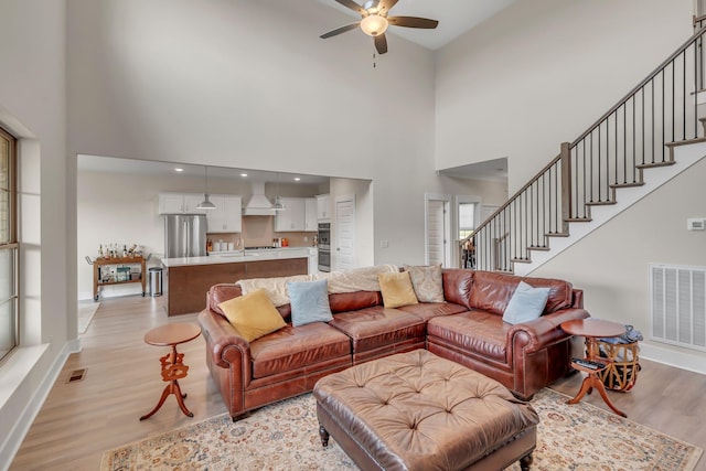 living room featuring a towering ceiling, light hardwood / wood-style flooring, and ceiling fan