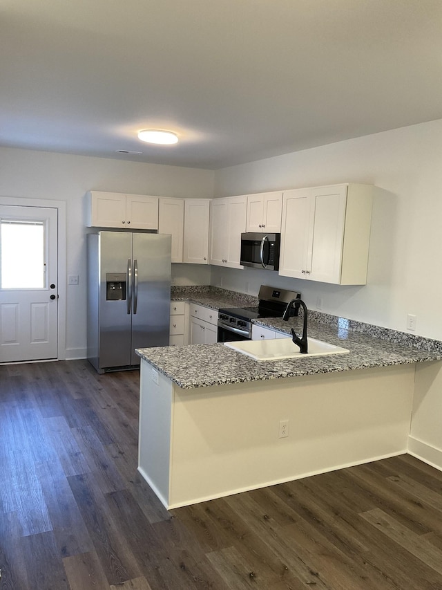 kitchen with light stone countertops, sink, stainless steel appliances, kitchen peninsula, and white cabinets