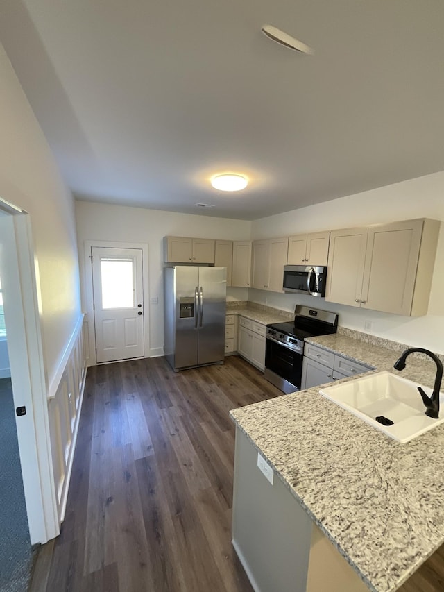 kitchen with light stone countertops, appliances with stainless steel finishes, dark hardwood / wood-style floors, and sink