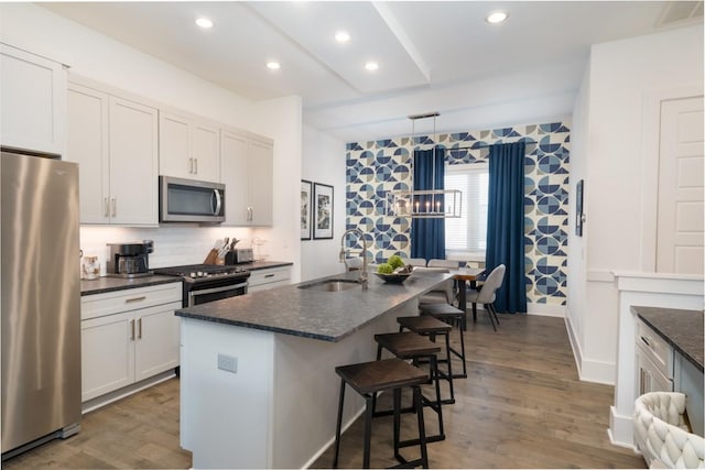 kitchen featuring appliances with stainless steel finishes, a center island with sink, white cabinetry, and pendant lighting