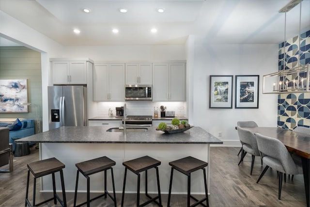 kitchen with appliances with stainless steel finishes, a breakfast bar, sink, a center island with sink, and white cabinetry