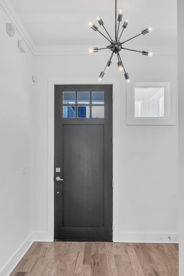 entrance foyer with crown molding, a notable chandelier, light wood-style floors, and baseboards