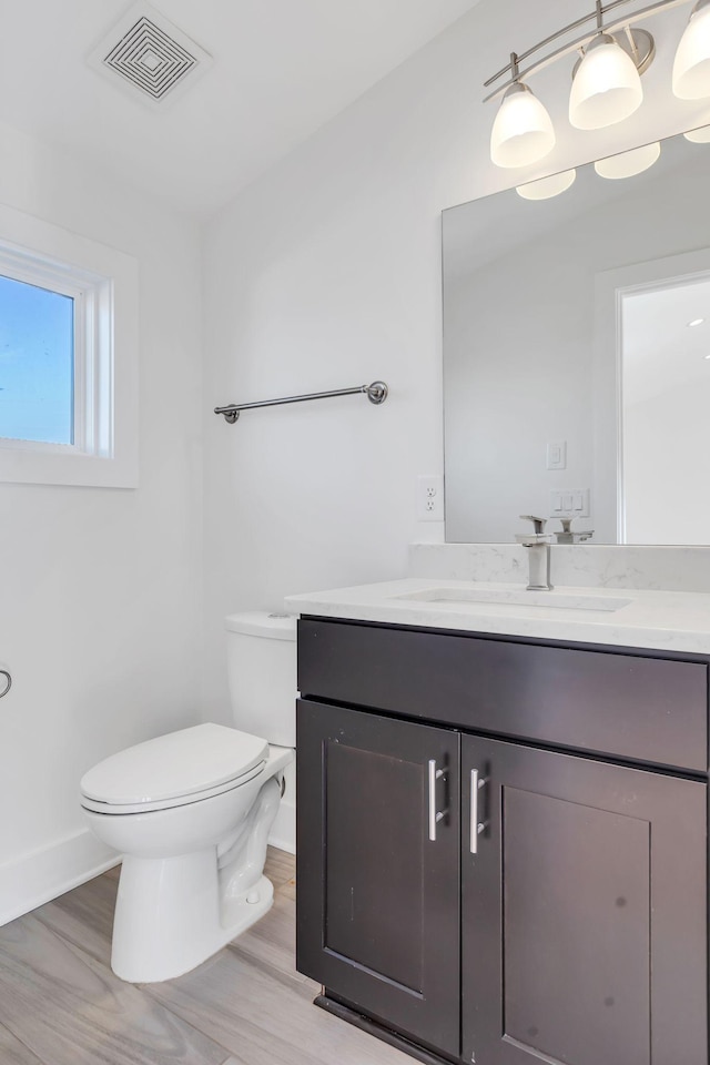 half bath with visible vents, toilet, wood finished floors, baseboards, and vanity