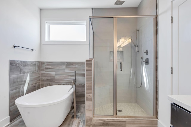 full bathroom with visible vents, a shower stall, tile walls, a soaking tub, and vanity