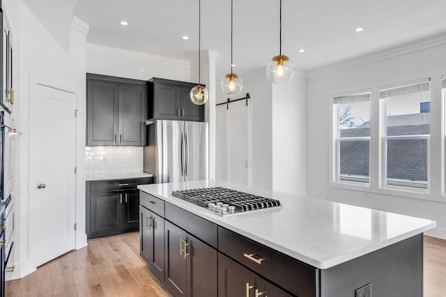 kitchen with light wood-style flooring, ornamental molding, tasteful backsplash, a barn door, and appliances with stainless steel finishes