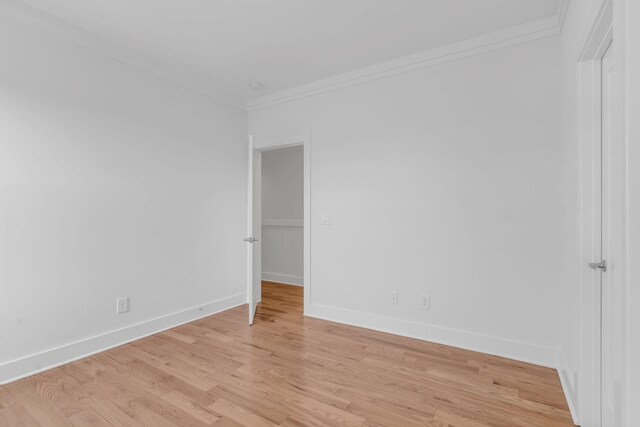 empty room featuring crown molding, light wood-type flooring, and baseboards