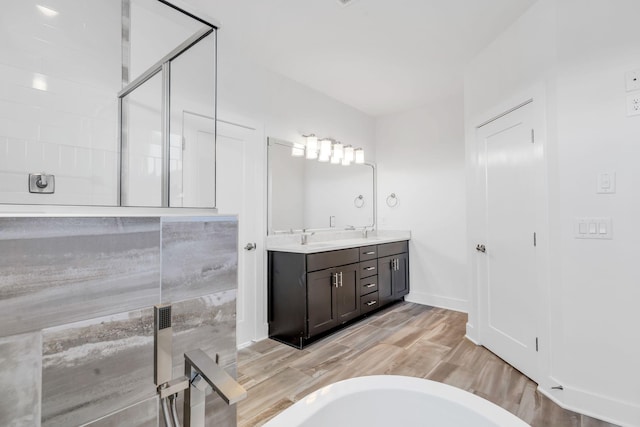 bathroom with a shower with door, wood finished floors, double vanity, a freestanding tub, and a sink