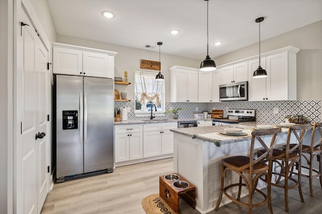 kitchen with white cabinetry, a breakfast bar, stainless steel appliances, and decorative light fixtures