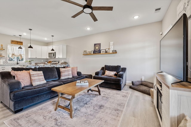 living room featuring ceiling fan, light hardwood / wood-style flooring, and sink