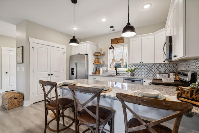 kitchen featuring appliances with stainless steel finishes, sink, light hardwood / wood-style floors, white cabinetry, and hanging light fixtures