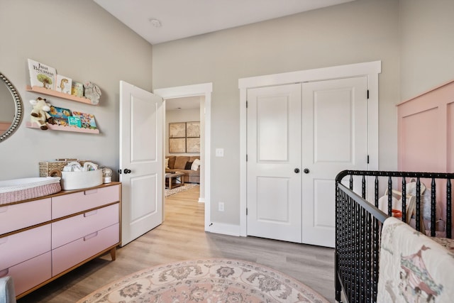 bedroom with a closet, light hardwood / wood-style floors, and a crib