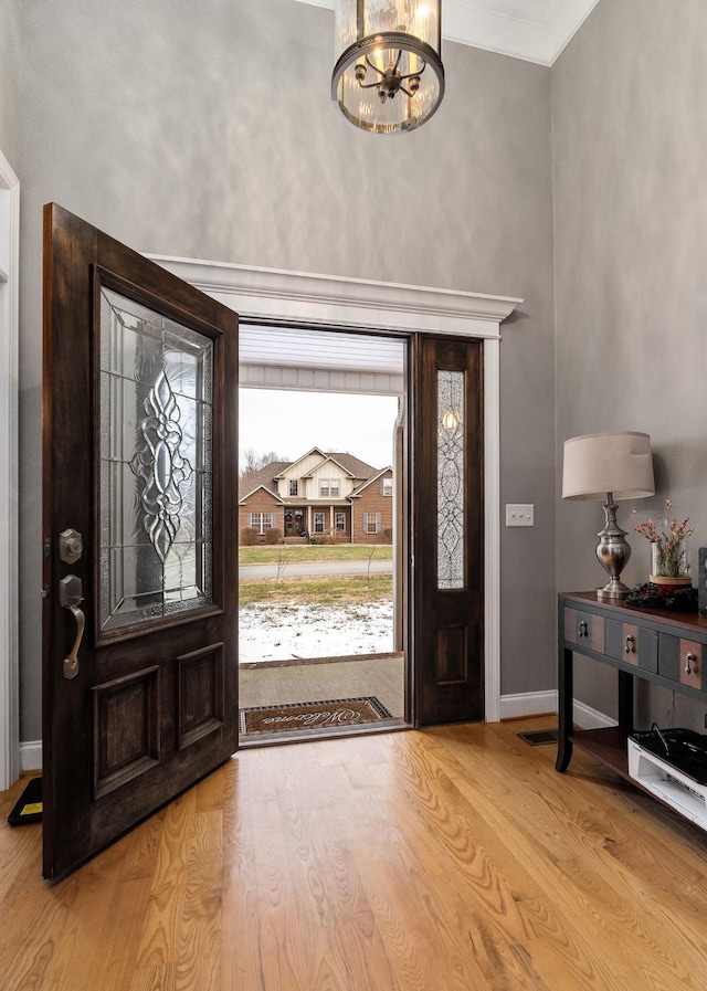 entryway with light wood-type flooring, an inviting chandelier, and crown molding