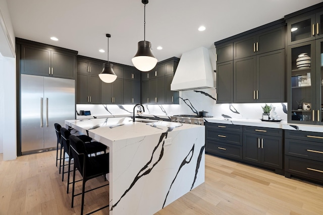 kitchen featuring stainless steel built in refrigerator, pendant lighting, a spacious island, light hardwood / wood-style floors, and custom range hood