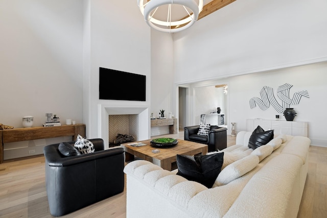 living room featuring beam ceiling, light hardwood / wood-style flooring, a towering ceiling, and an inviting chandelier