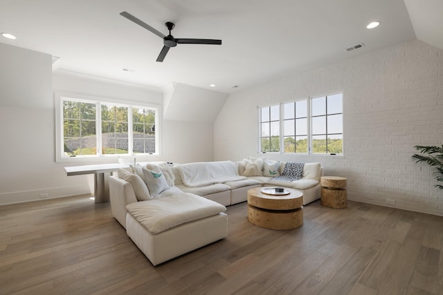 living room featuring hardwood / wood-style flooring, ceiling fan, lofted ceiling, and brick wall