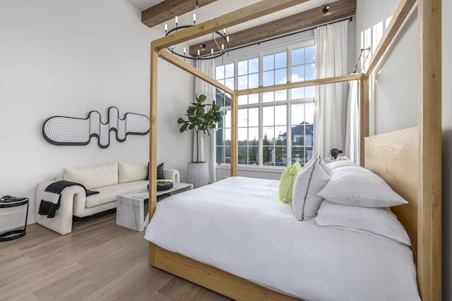 bedroom featuring beamed ceiling, light hardwood / wood-style floors, and a chandelier