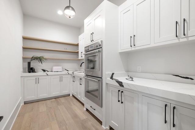 kitchen featuring light stone countertops, stainless steel double oven, light hardwood / wood-style floors, white cabinetry, and hanging light fixtures