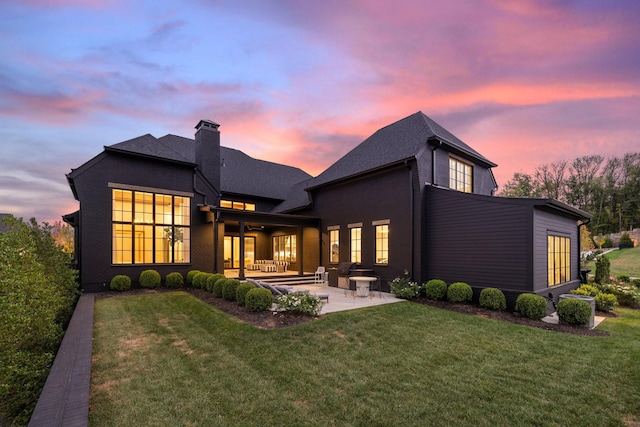 back house at dusk with a patio area and a yard