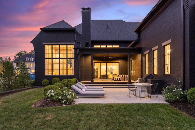 back house at dusk featuring ceiling fan, a yard, and a patio