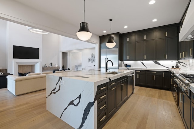 kitchen with premium range hood, light stone counters, pendant lighting, light hardwood / wood-style floors, and an island with sink