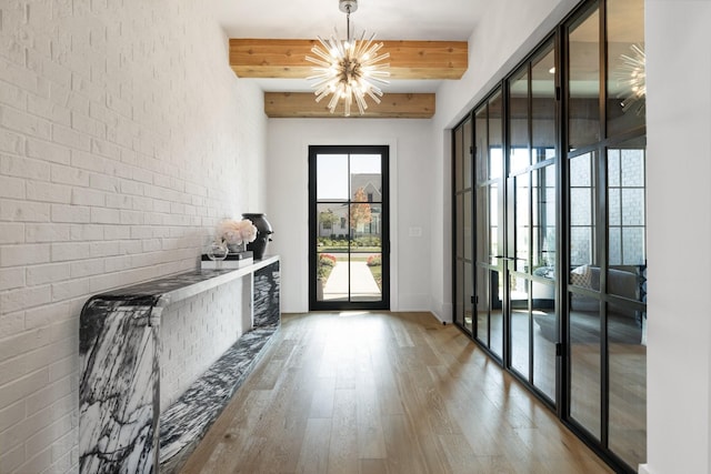 doorway featuring hardwood / wood-style floors, french doors, beam ceiling, brick wall, and a chandelier