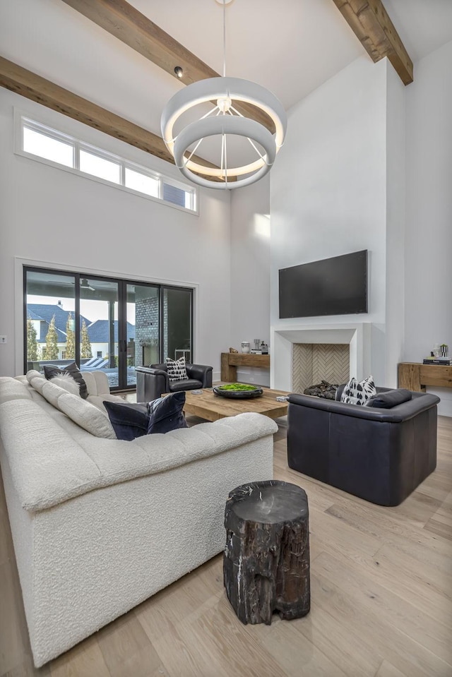 living room featuring beam ceiling, wood-type flooring, a high ceiling, and a chandelier