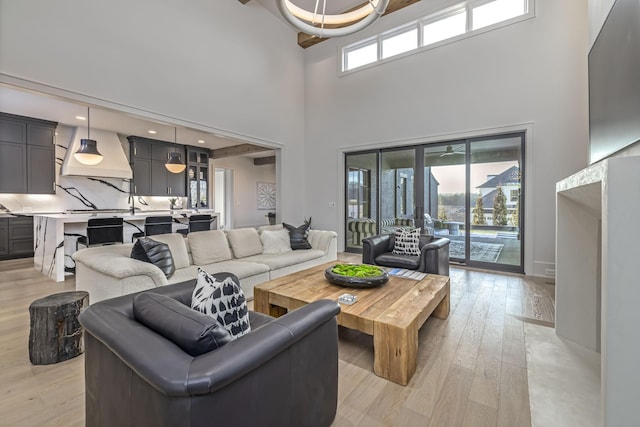 living room featuring a towering ceiling, light wood-type flooring, and beam ceiling