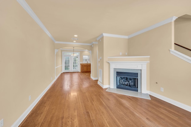 unfurnished living room with an inviting chandelier, ornamental molding, and light hardwood / wood-style flooring