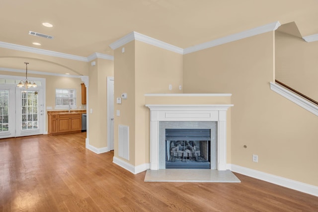 unfurnished living room featuring light hardwood / wood-style floors, ornamental molding, sink, and a chandelier